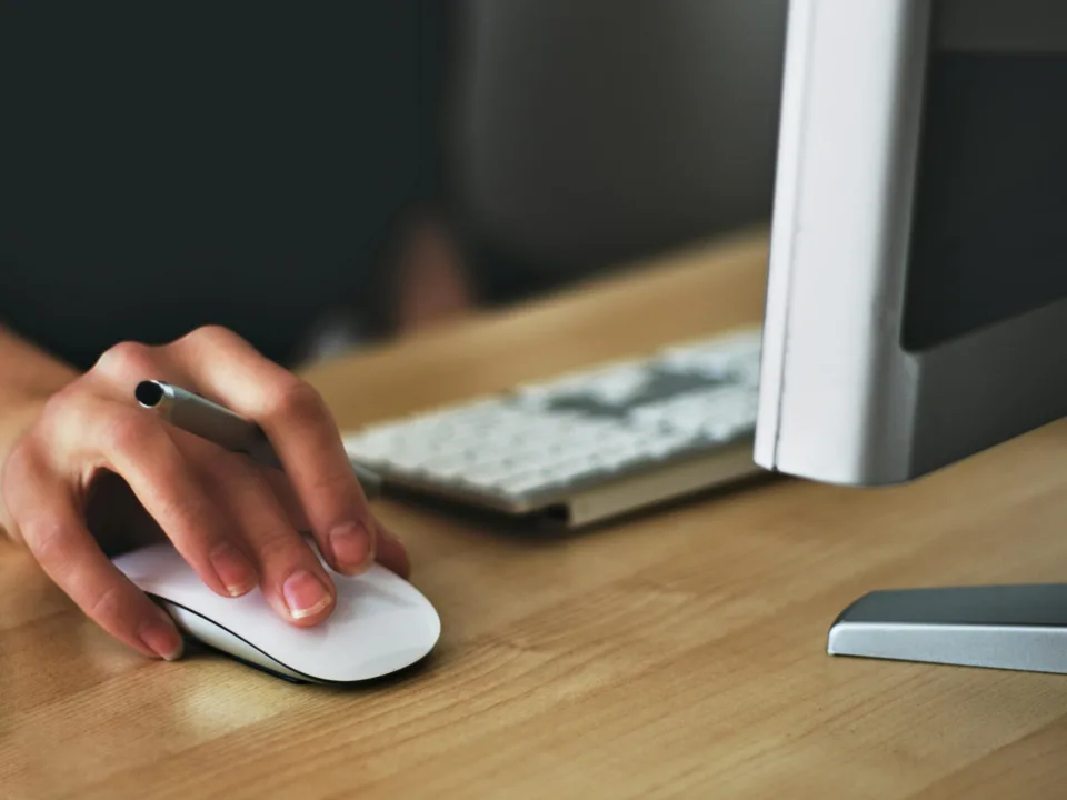 Free A hand using a wireless mouse at a modern desk setup with a computer and keyboard. Stock Photo